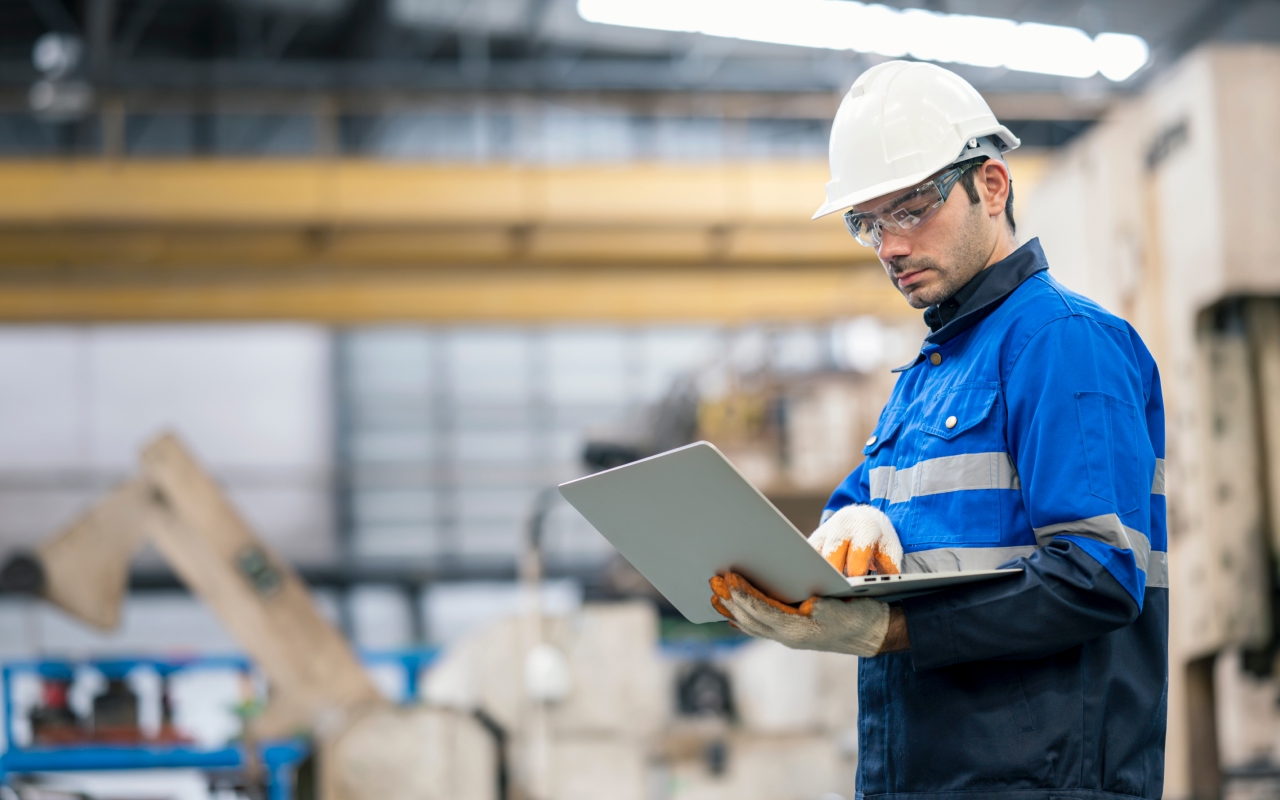 Occupational safety professional wearing a white helmet and blue jacket, using a laptop